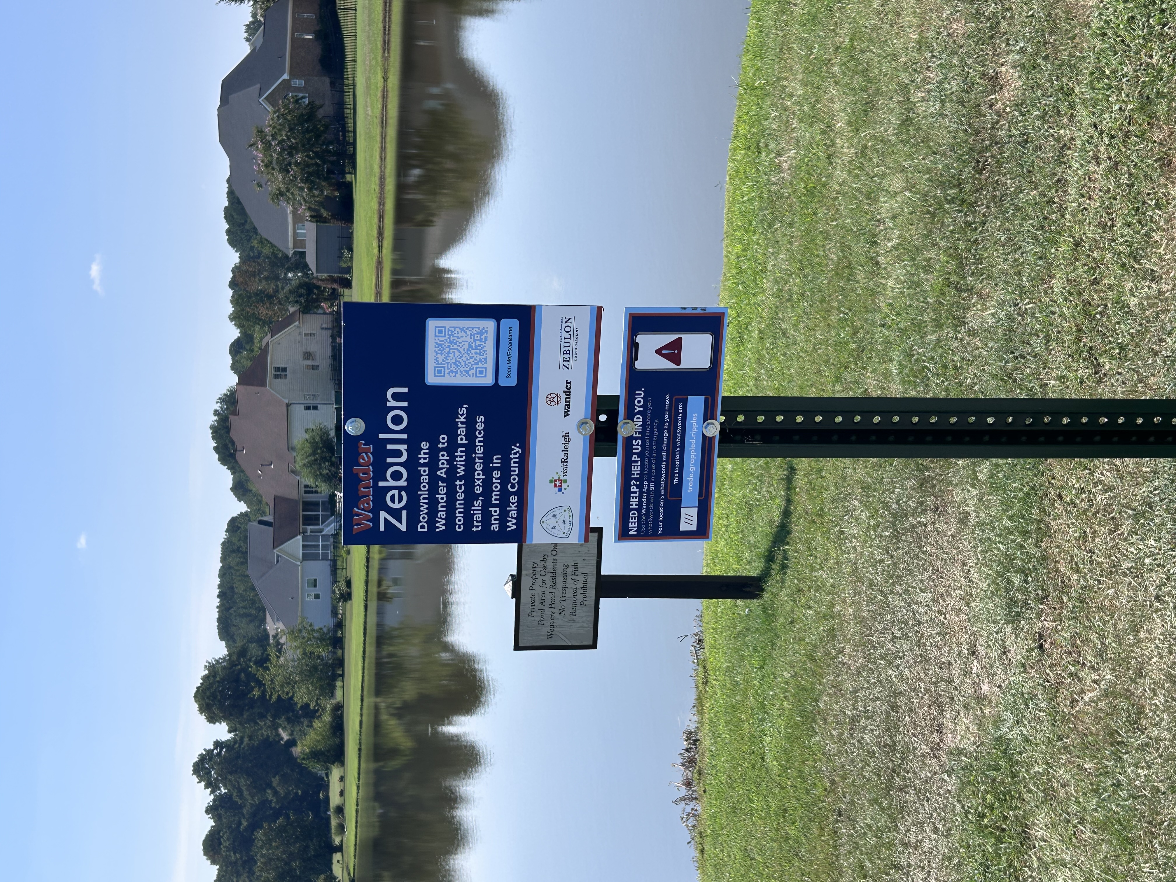 An installed Wander Zebulon sign beside a neighborhood pond, with a separate notice identifying the pond as private property.